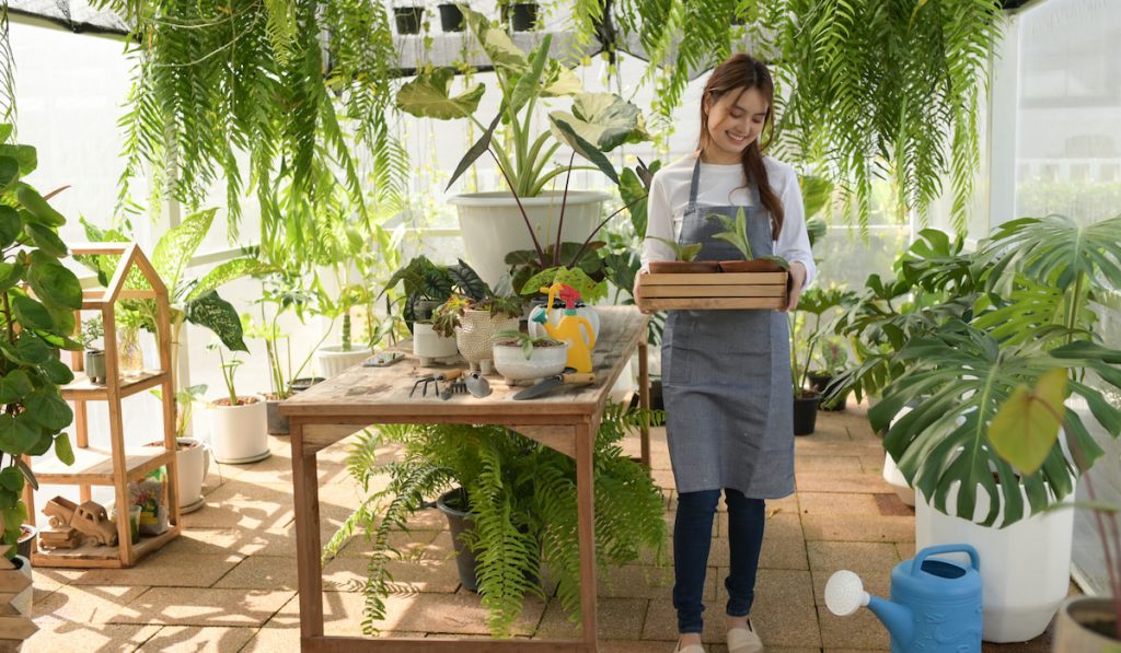 A girl in an apron works in a greenhouse planting trees.