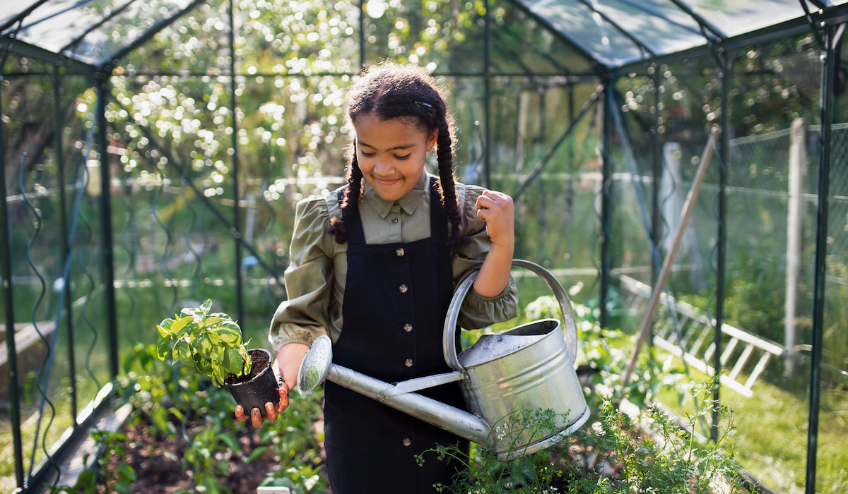 Happy-small-girl-gardening-in-greenhouse-outdoors-in-backyard