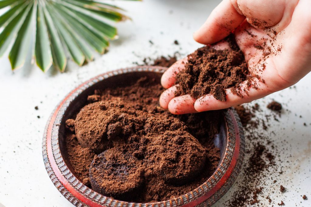 Woman's hand crumbles coffee grounds into wooden bowl.